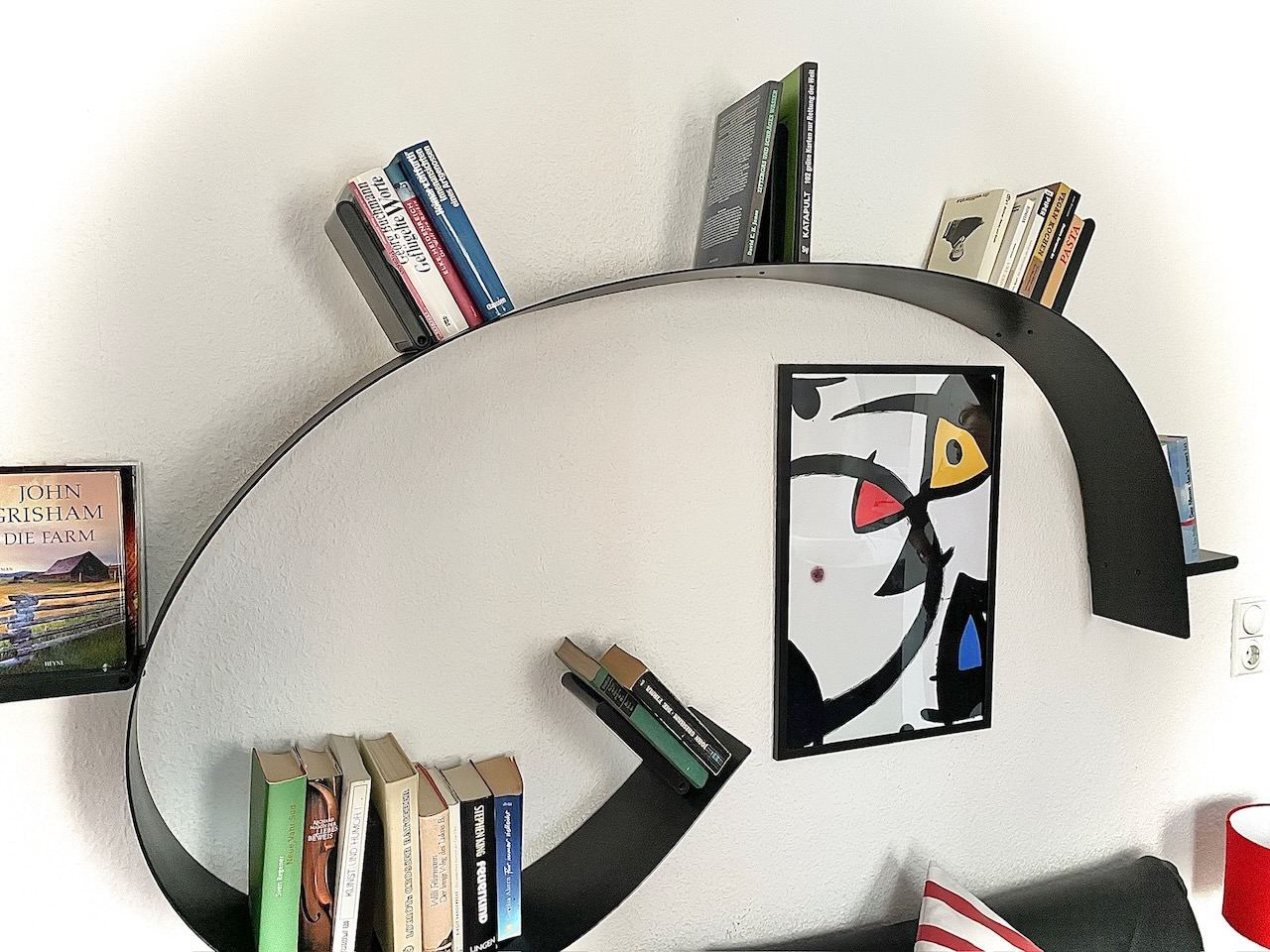 Geschwungenes Bücherregal mit Romanen und einem Miró-Druck