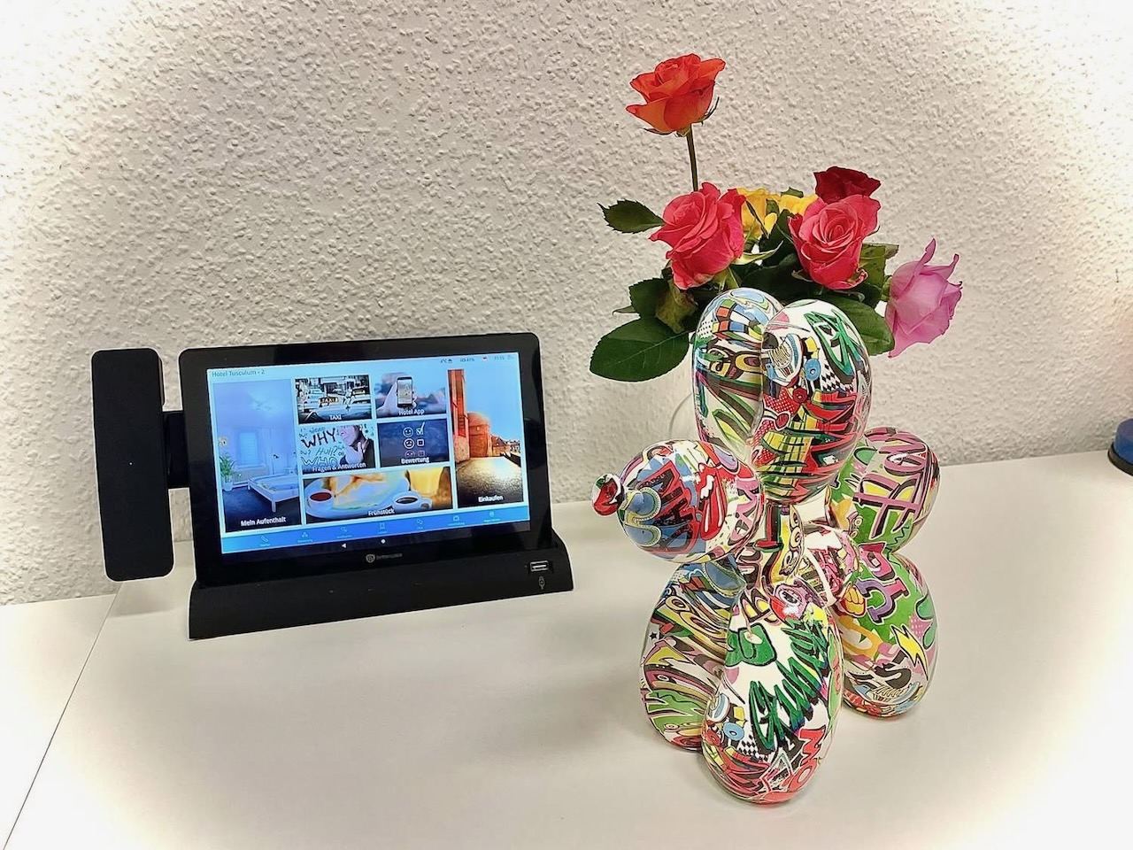 Tablet mit Zimmerinformationen neben einer Vase mit Rosen