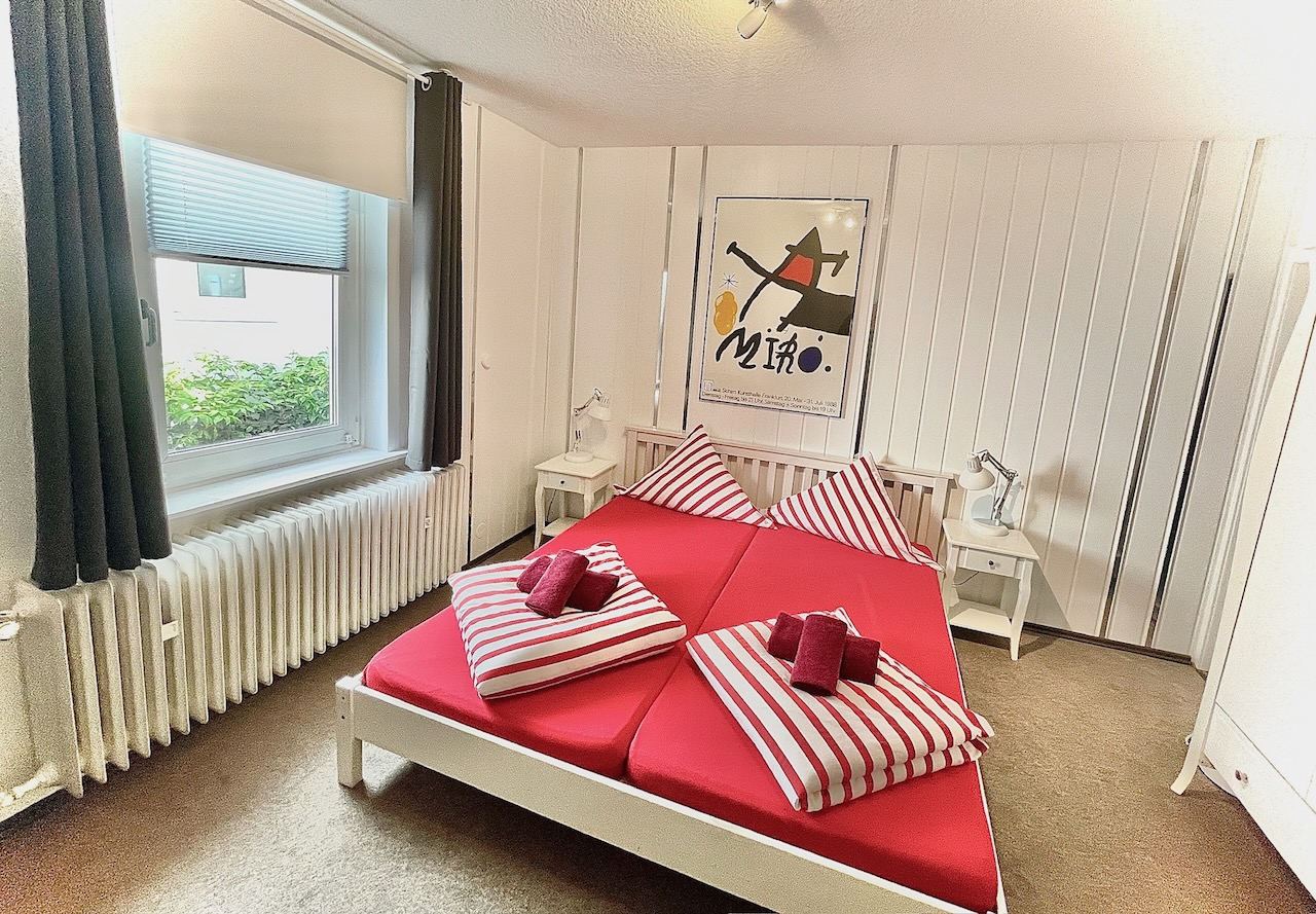 Doppelzimmer mit rot bezogenem Bett am Fenster