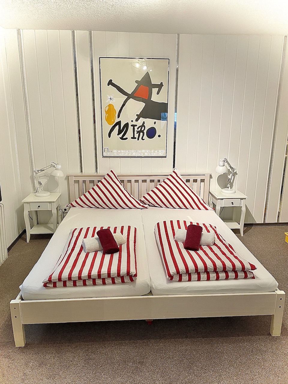 Doppelzimmer mit rot-weiß gestreifter Bettwäsche unter einem Miró-Plakat