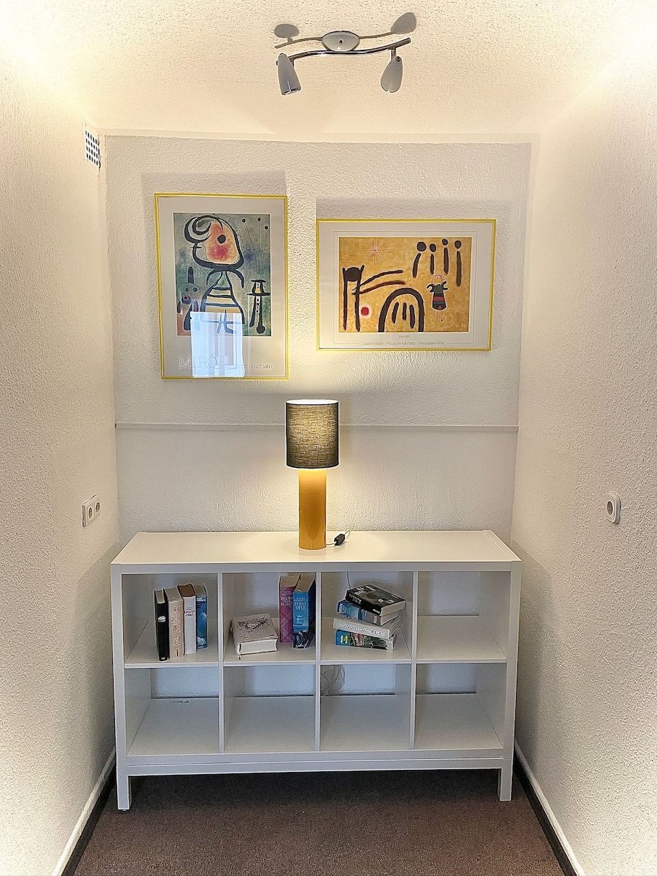 Bücherregal mit Leselampe unter zwei gerahmten Grafiken