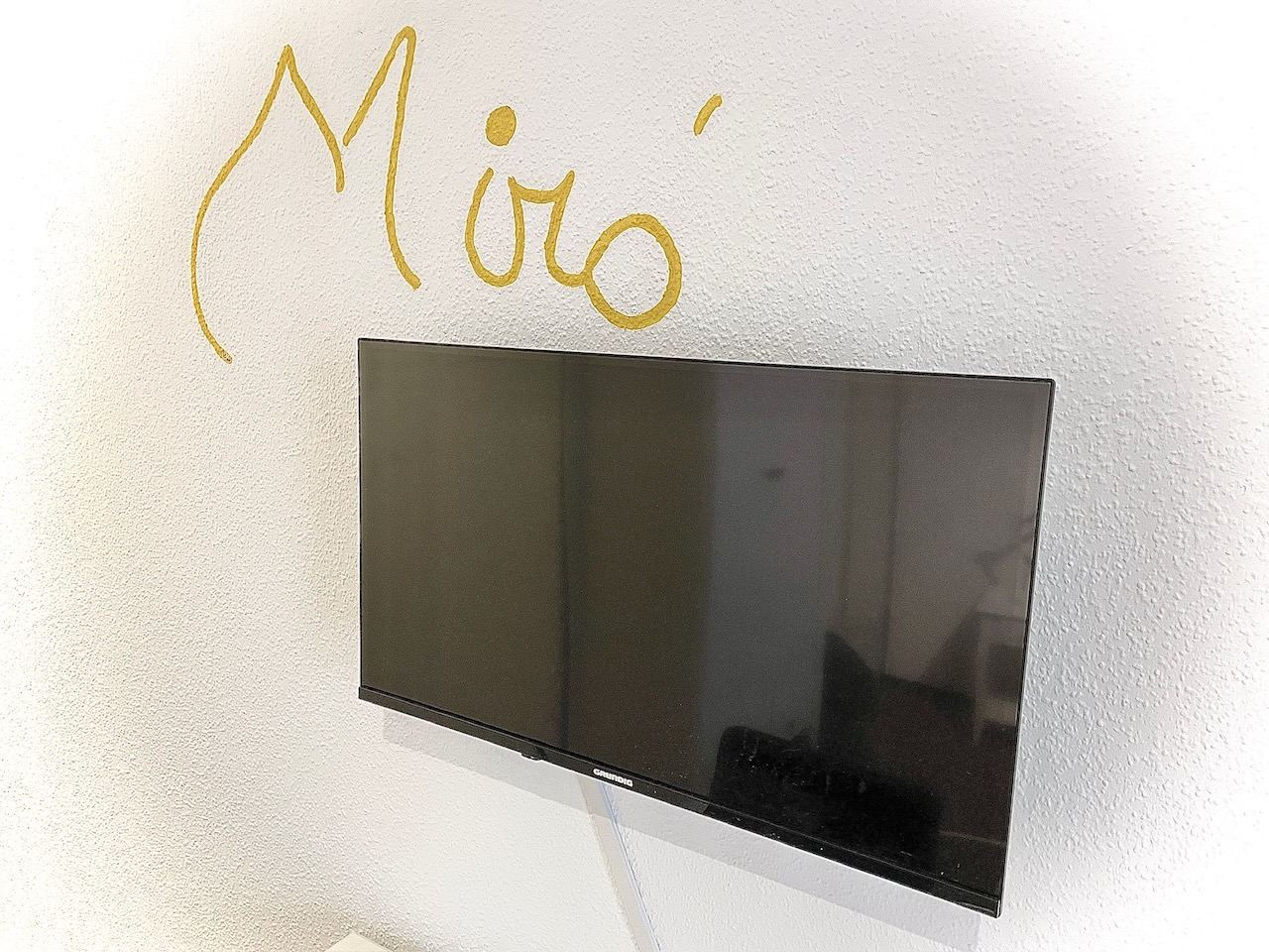 Flachbild-TV an der Wand neben einem gemalten Miró-Schriftzug
