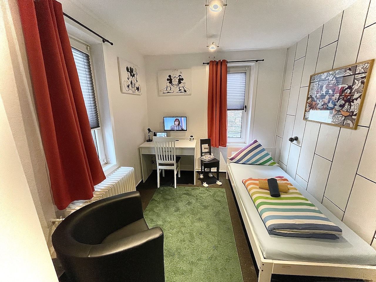 Zimmer mit roten Vorhängen, Bett, Sessel und Arbeitsplatz