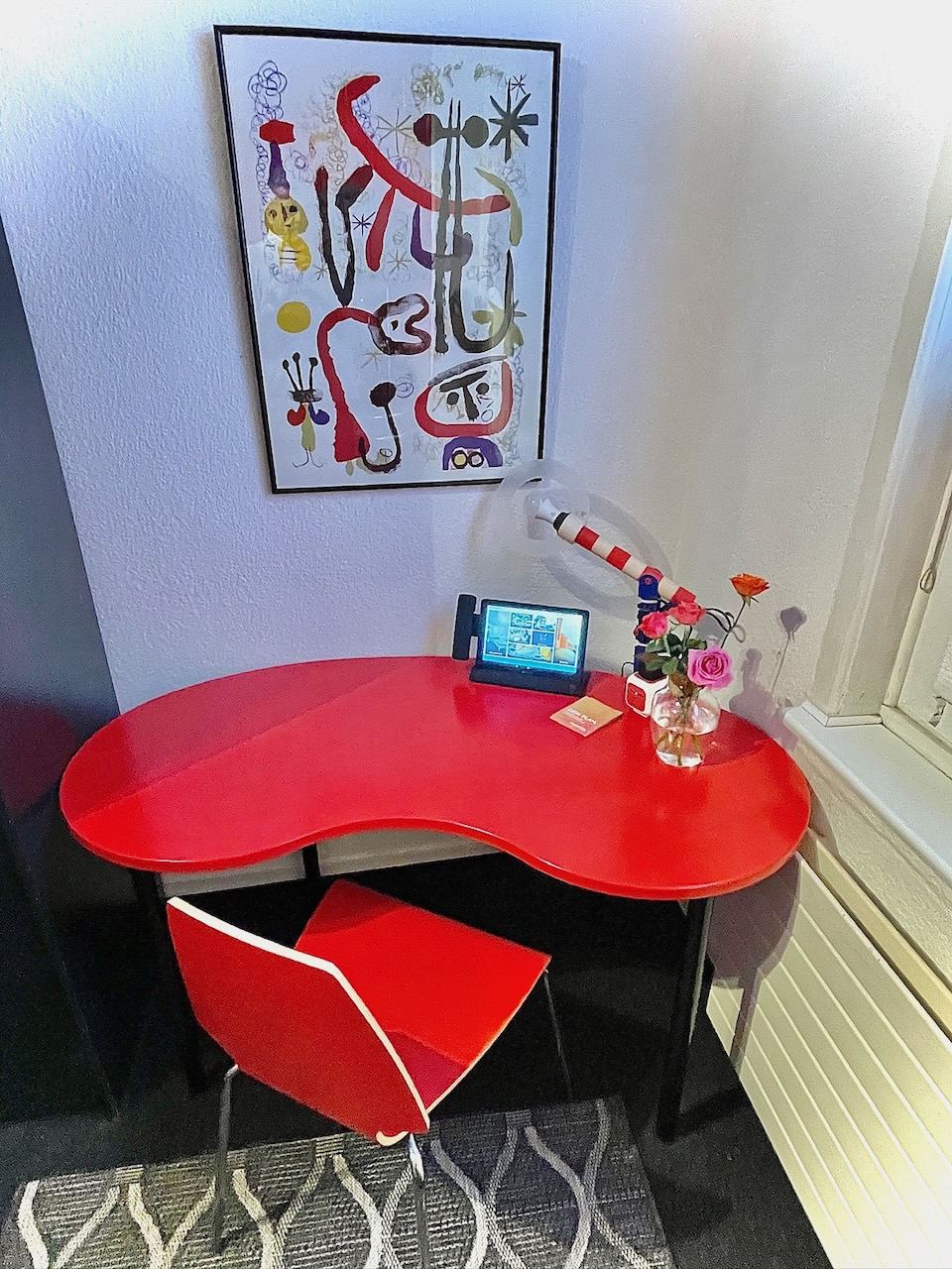 Roter Nierentisch mit Schreibtischlampe und Blumen im Einzelzimmer